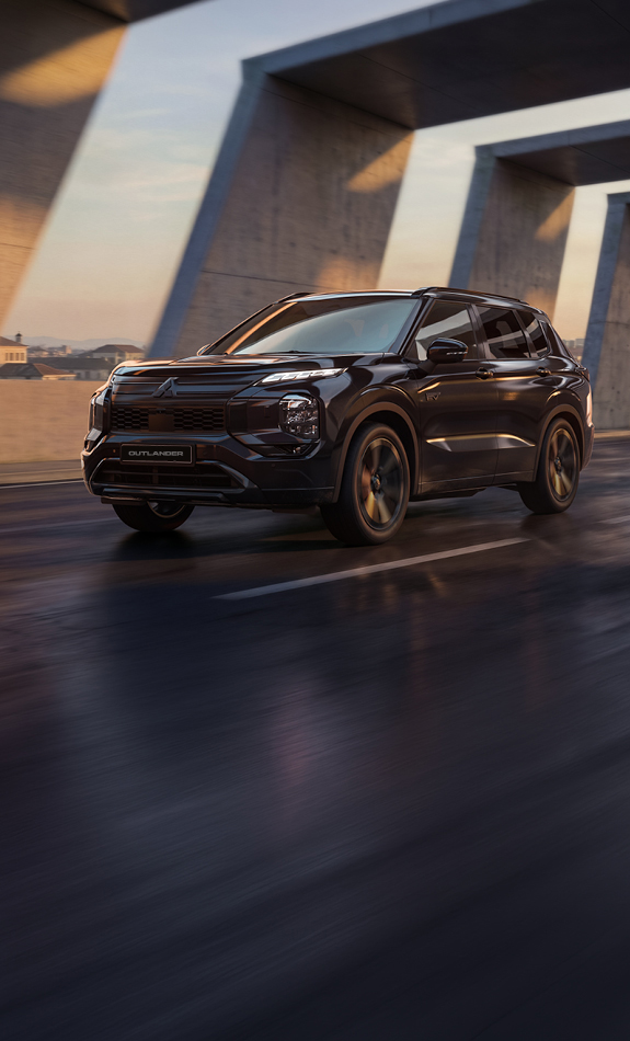 Schwarzer Mitsubishi Outlander Black in dynamischer Frontansicht unter einer modernen Betonbrücke bei Sonnenuntergang